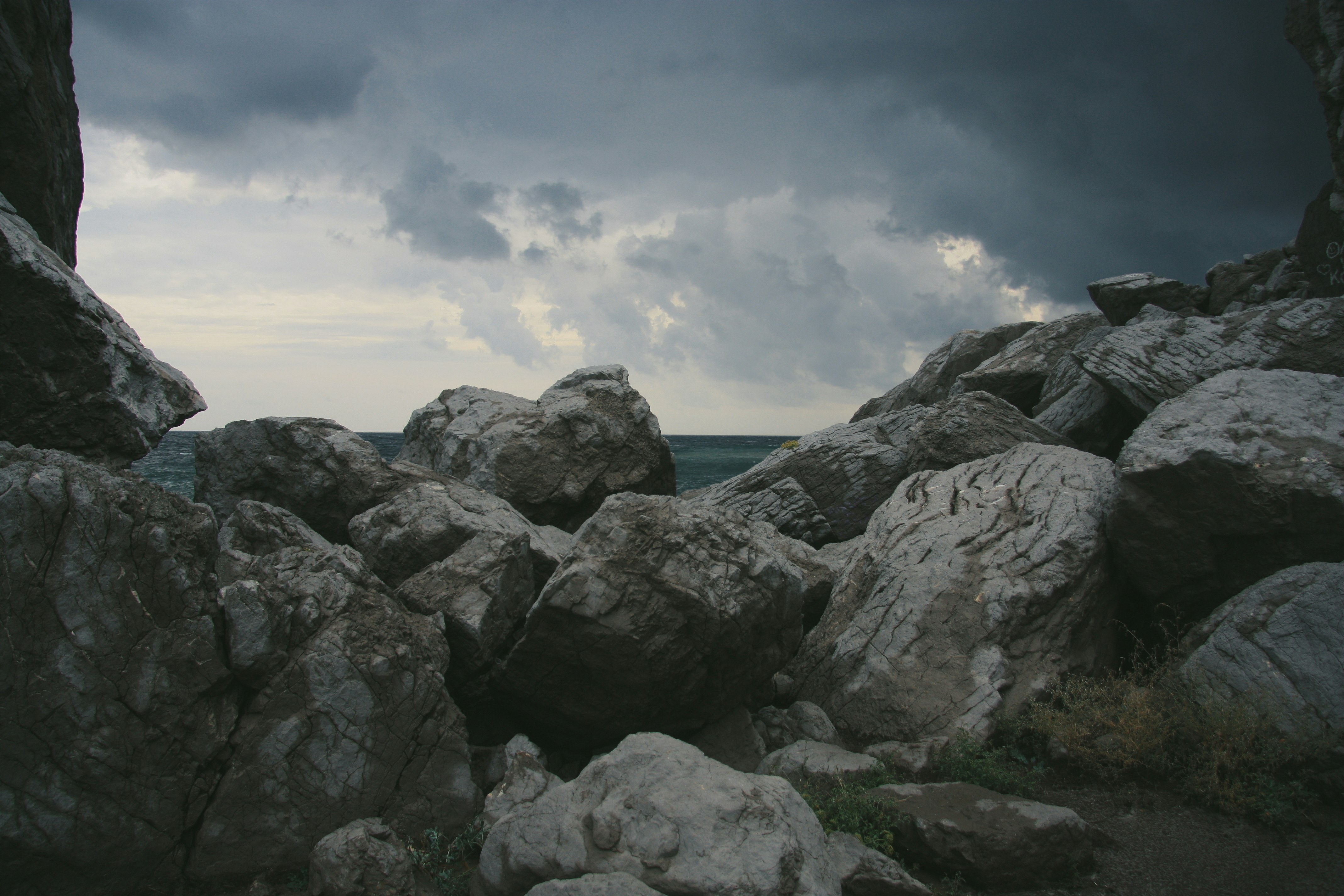 gray rocky mountain near body of water under white clouds during daytime